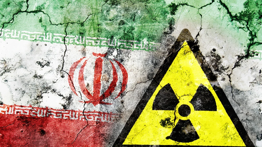Illustrative: Old cracked wall with radiation warning sign and painted flag, flag of Iran. Credit: MyImages-Micha/Shutterstock.