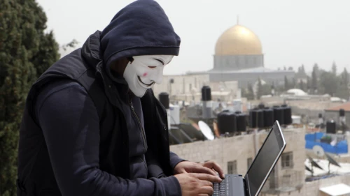 A Palestinian youth wearing masks used by computer hackers who attacked a number of Israeli websites recently, seen backdropped by the Temple Mount in Jerusalem's Old City, April 8, 2013. Photo by Sliman Khader/Flash90.
