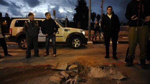 Israelis stand near a hole caused by a Palestinian rocket fired from Gaza into the southern Israeli city of Sdeort on March 12, 2014. At least 60 Islamic Jihad rockets were launched from Gaza at Israel from March 12-13. Credit: Flash90.