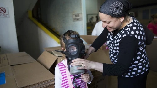 An Israeli woman shows her child how to put on a gas mask at a distribution center in Jerusalem on August 27, 2013. As talks of an international attack on Syria heighten, the demand for gas masks in Israel rose. Credit: Yonatan Sindel/Flash90.
