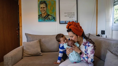 Israel Defense Forces widow Revital Shamir, her 4-year-old son and newborn baby girl sit underneath a painting of her late husband, Maj. Mordechai Shamir, at their home in Yair's Farm in Samaria, Feb. 21, 2024. Photo by Chaim Goldberg/Flash90.