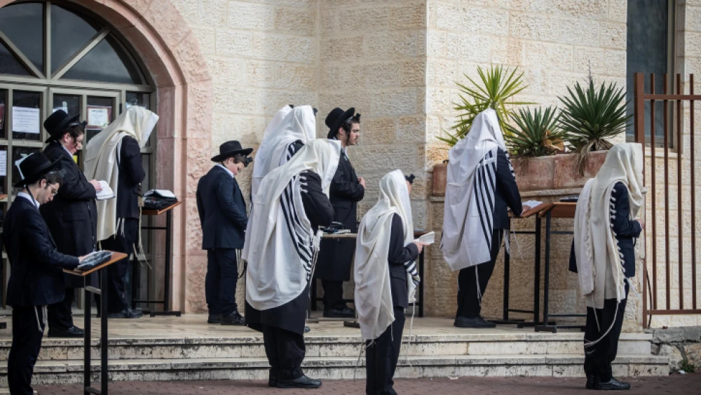 Jewish men pray outside a synagogue in the city of Beitar Illit in Judea and Samaria, on March 29, 2020. Photo by Aharon Krohn/Flash90.