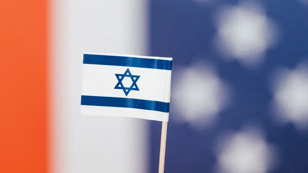 A small Israeli flag against a blurred American flag background. Credit: Kaboom Pics/Pexels.