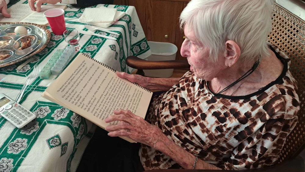 An elderly woman who has low vision reads from a large print haggadah at her family Passover seder.