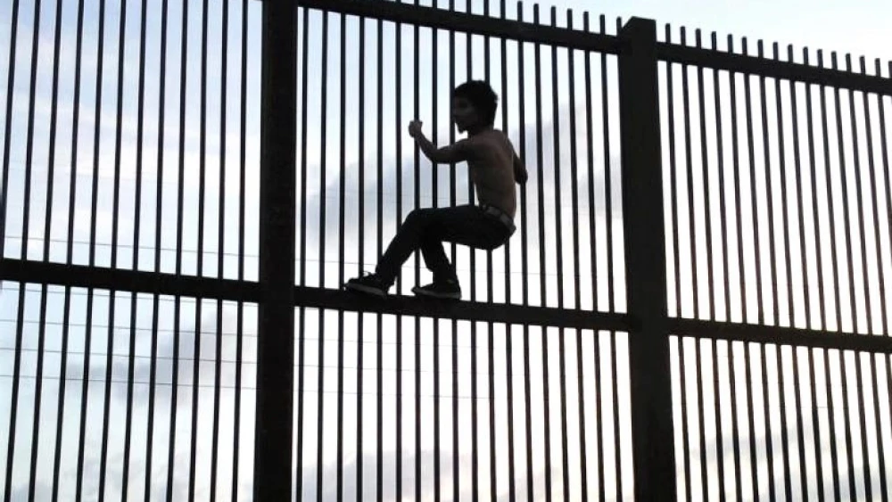 An immigrant attempting to cross the U.S.-Mexico border by illegally by climbing over the border fence in Brownsville, Texas in July 2009. Credit: Nofx221984 via Wikimedia Commons.