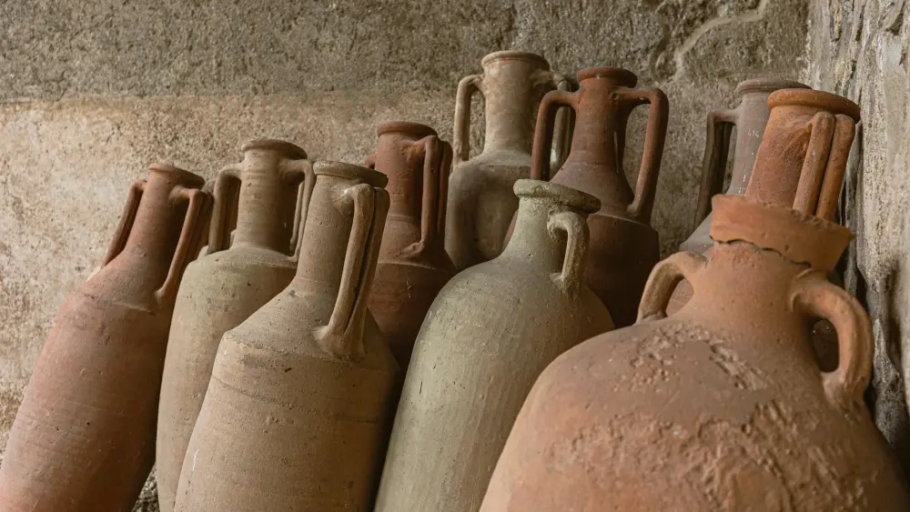 Rustic clay jars arranged against a textured stone wall. Credit: James Frid/Pexels.