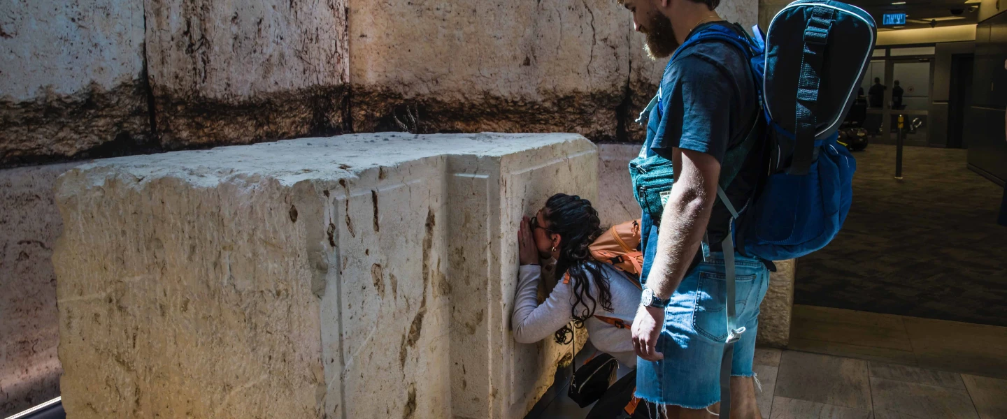 Shelly Sarah, a 22 year old Israeli from Hadera, stops at the Western Wall stone on display at Israel's Ben-Gurion International airport before a trip to Thailand as her boyfriend looks on, March 25, 2025. Credit: Rina Castelnuovo.
