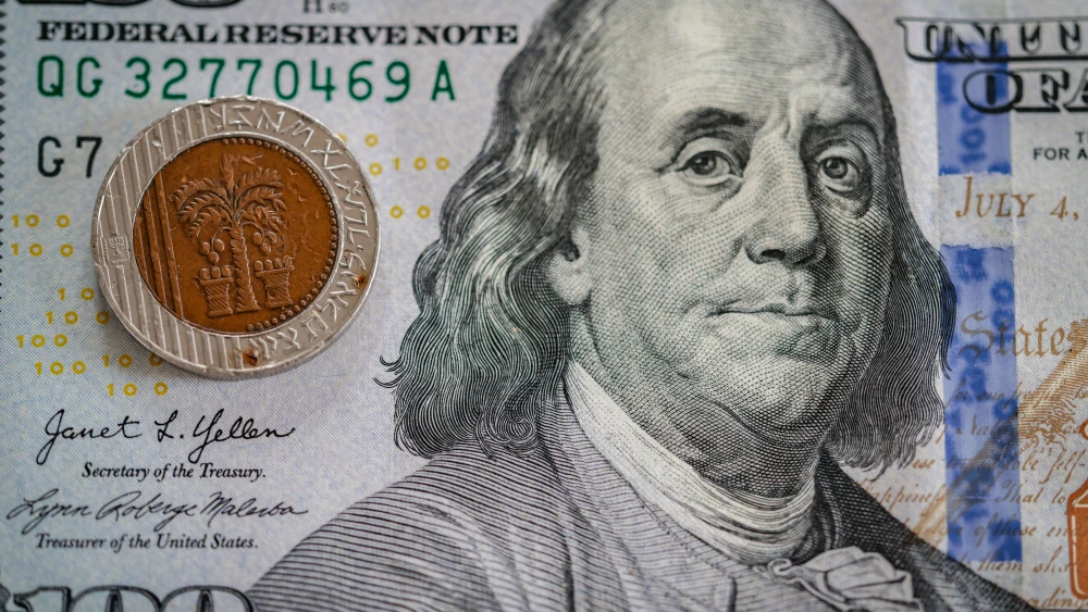 Illustration photo of a 10 shekel coin placed on a US 100 dollar bill, May 9, 2026. Photo by Nati Shohat/Flash90.