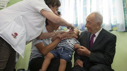 Then-Israeli President Shimon Peres (right), whose son has contracted and overcome Polio, watches as a medical worker administers a dose of a Polio immunization to a young boy at a clinic in Jerusalem on Aug. 21, 2013. Israel's Health Ministry initiated a mass vaccination program for more than 1 million children in Israel following the recent discovery of the Polio virus in sewer systems. Credit: Flash 90.