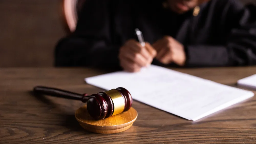A judge signing a document in a courtroom setting. Credit: Katrin Bolovtsova/Pexels.