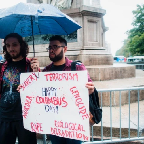 Two protesters display a placard under the statue of Christopher Columbus at the Columbus Circle in New York on Oct. 9, 2017, calling for the removal of the statue. Credit: JEWEL SAMAD/AFP/Getty Images.