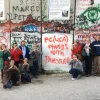 Members of the Presbyterian Church USA's Israel Palestine Mission Network pose in front of Israel's security barrier during one of their trips to the Holy Land. The graffiti on the barrier readers “PC(USA) stands with Palestine.” Source: Twitter.