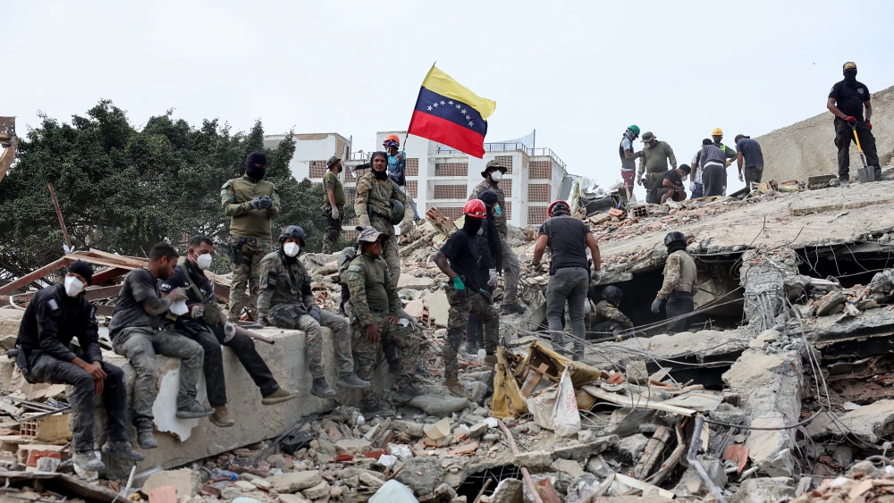 Rescuers search for victims at a collapsed building as one raises a Venezuelan flag following a magnitude 7.2 earthquake that struck Venezuela and other regions in the Caribbean, on June 28, 2026, in Carabellada, Venezuela. Photo by Jesus Vargas/Getty Images.