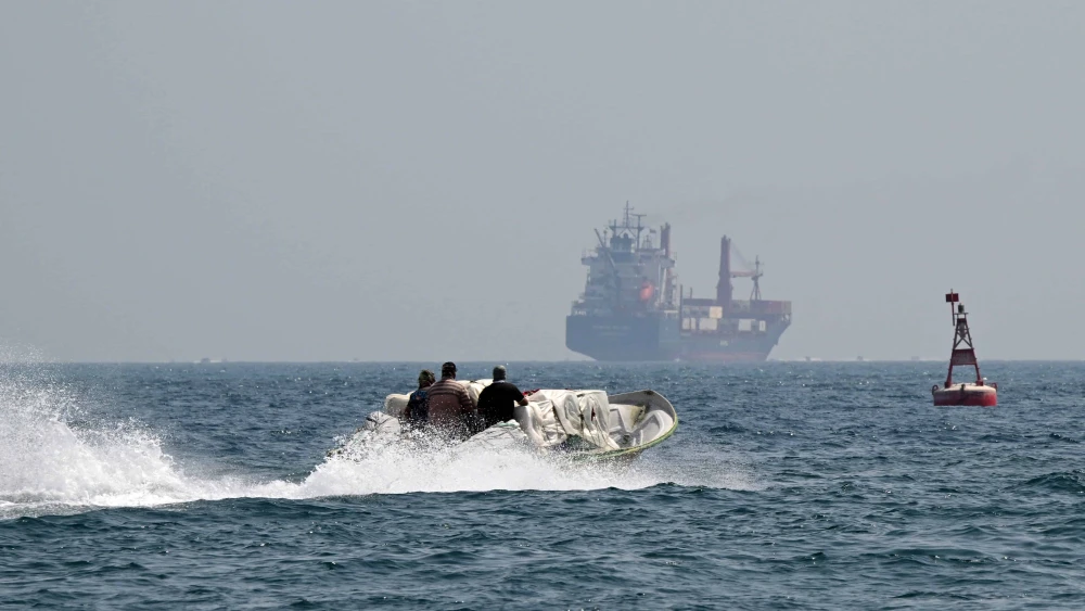 A small boat loaded with merchandise sails past the St Kitt's and Nevis-flagged container ship Marsa Victory in the waters of the Strait of Hormuz off the coast of Khasab in Oman's northern Musandam peninsula on June 25, 2025. Photo by Giuseppe Cacace/AFP via Getty Images.