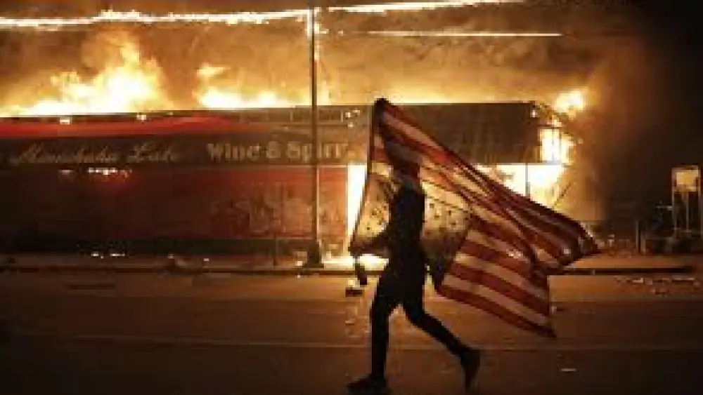A protester flies an upside-down American flag through the streets of one of the cities beset by riots in the wake of the killing of George Floyd by Minneapolis police officers on May 29, 2020. Source: Screenshot.