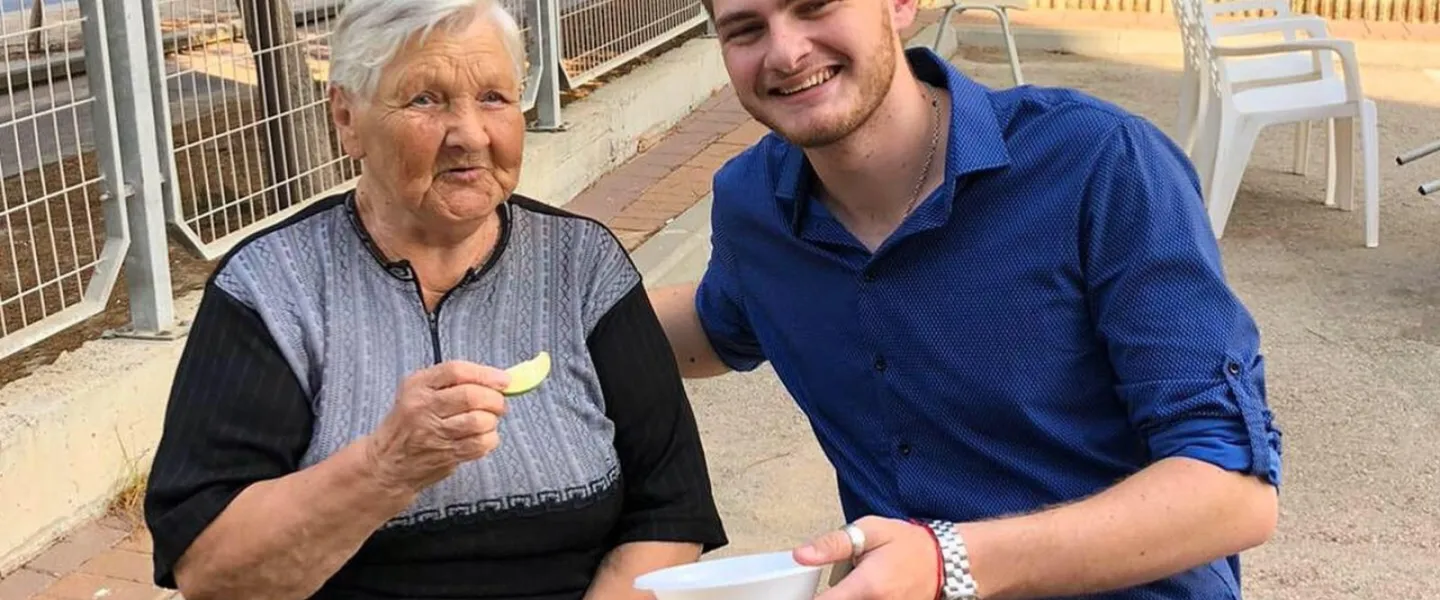 Yakov Pizenberg enjoys a snack with a senior citizen. Credit: Courtesy.