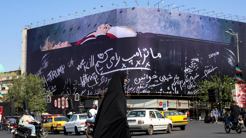 An Iranian woman walks past a giant propaganda poster showing U.S. President Donald Trump in a coffin with text reading "We Kill Trump" in Tehran's Revolution Square, July 15, 2026 Photo by AFP via Getty Images.