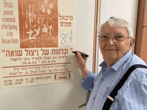Michael Smuss points to a poster commemorating the 50th anniversary of the Warsaw Ghetto Uprising in 1993. Credit: Courtesy.