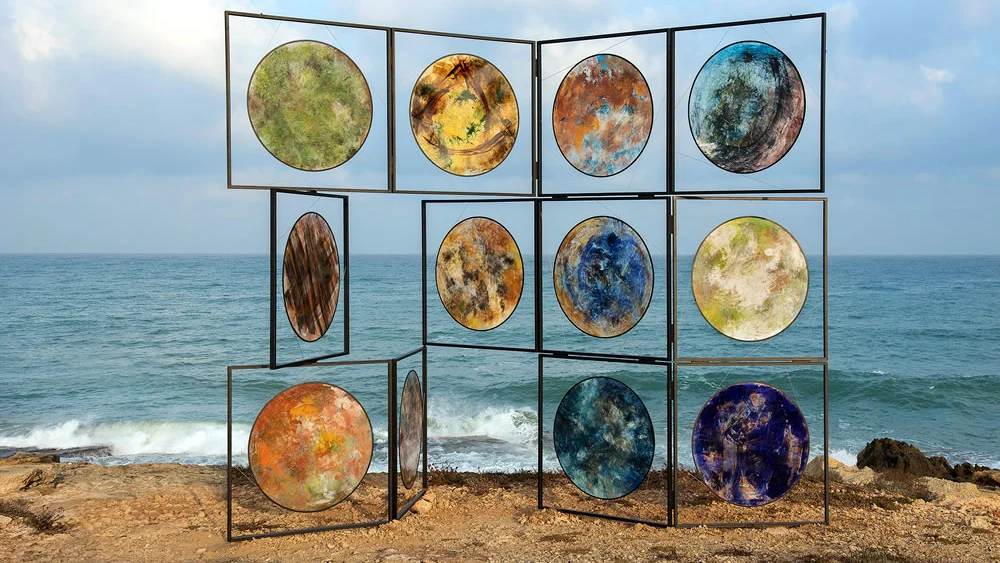 Twelve circular paintings on translucent PVC by artist Beverly Barkat on Achziv beach in Israel as part of “After the Tribes.” Credit: Photo by Michael Amar.