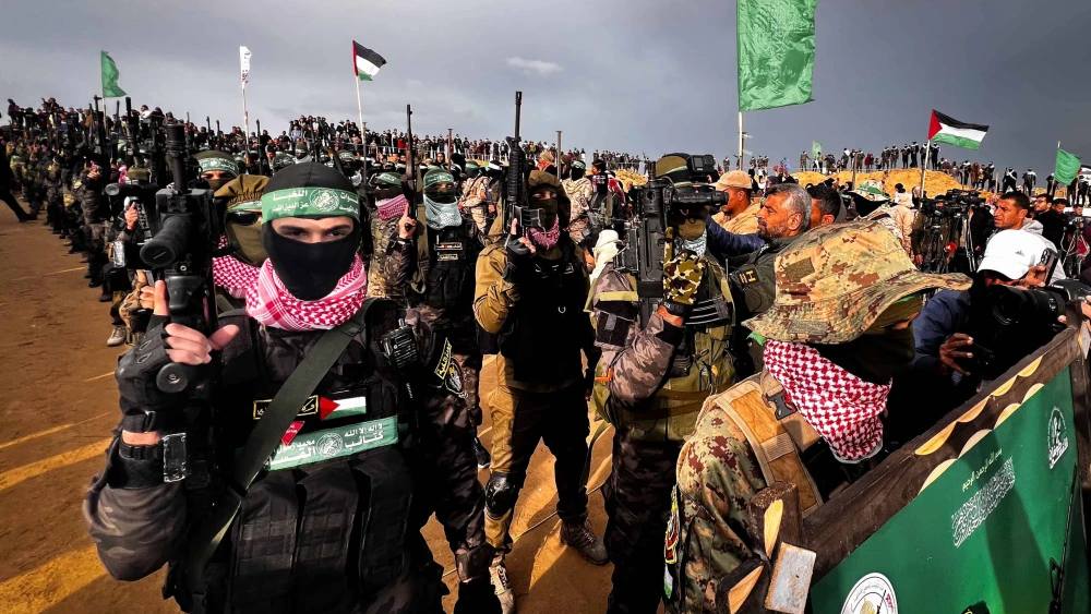 Al-Qassam Brigades terrorists stand guard while Palestinians wait for the handover of the bodies of four Israeli hostages to the Red Cross in Khan Yunis, the Gaza Strip, Feb. 20, 2025. Photo by Saeed Mohammed/Flash90.