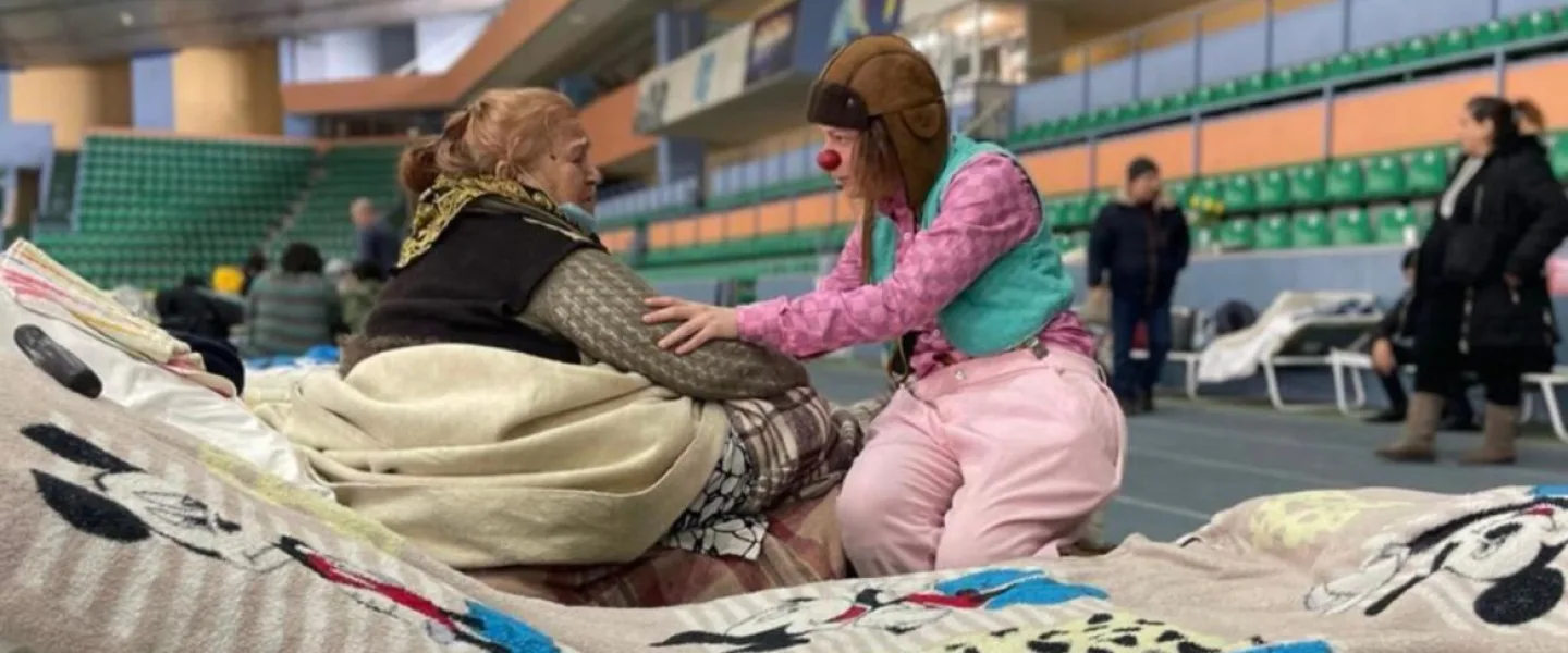 An Israeli medical clown comforting a displaced Ukrainian sheltering in a Moldovan stadium. Photo courtesy of Dream Doctors.