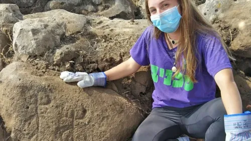 Ofri Eitan of the Kfar Hanasi pre-military academy next to the engraved stone at the site of the ancient fortified building complex uncovered in the Golan Heights, November 2020. Credit: Tidhar Moav/Israel Antiquities Authority.