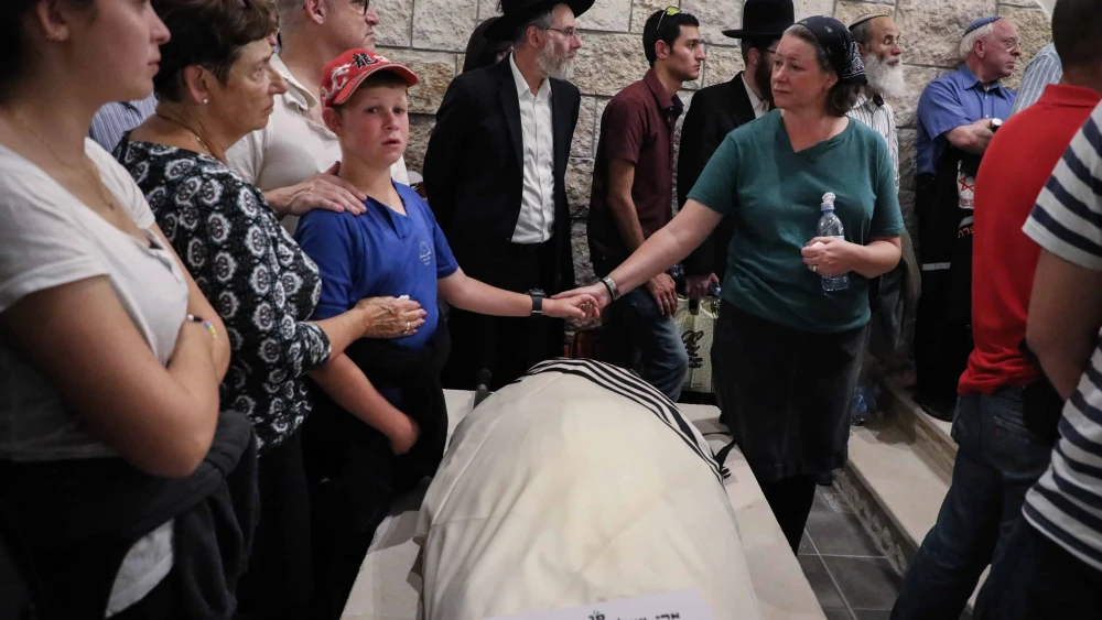 Ari Fuld's wife, Miriam, and son hold hands over his enshrouded body, wrapped in a tallit and awaiting burial at the Kfar Etzion cemetery in Judea. Photo by Gershon Elinson/Flash90.