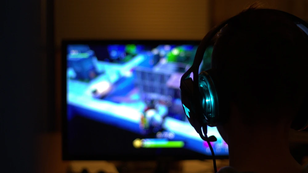 A person wearing a gaming headset while playing Fortnite on a computer monitor. Credit: Pixabay.