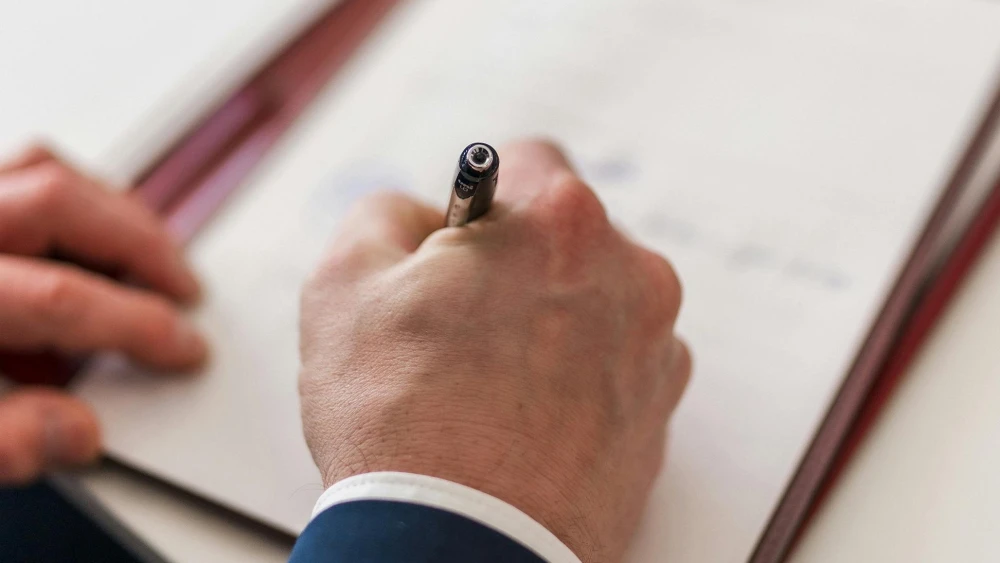 A man signing a document. Credit: Masood Aslami/Pexels.