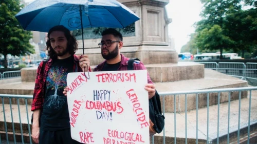 Two protesters display a placard under the statue of Christopher Columbus at the Columbus Circle in New York on Oct. 9, 2017, calling for the removal of the statue. Credit: JEWEL SAMAD/AFP/Getty Images.