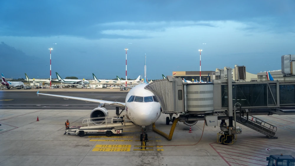 Airport employees finish loading luggage and an airport jetway or boarding bridge attached to a Eurowings low-cost airline plane parked on the tarmac at Rome Fiumicino Airport at dusk in Rome, Italy on June 18, 2025. Photo by Antoine Boureau / Hans Lucas / AFP via Getty Images.