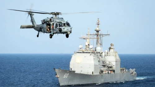 An HH-60H Sea Hawk helicopter passes the guided-missile cruiser “USS Normandy” in the Arabian Gulf in September 2015. Credit: Anna Van Nuys/U.S. Navy.