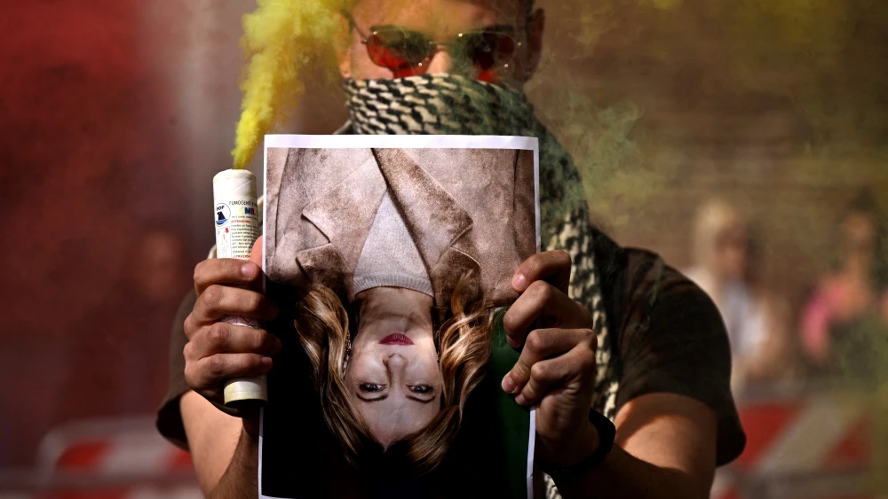 A demonstrator holding a smoke bomb and an upside-down portrait of Italy's Prime Minister Giorgia Meloni takes part in a protest against the Middle East war in Rome, March 28, 2026. Photo by Tiziana Fabi/AFP via Getty Images.