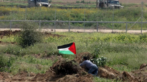A Palestinian man waves the Palestinian flag near Israeli soldiers by the border fence near Gaza City in March 2010. Photo by Wissam Nassar/Flash90.