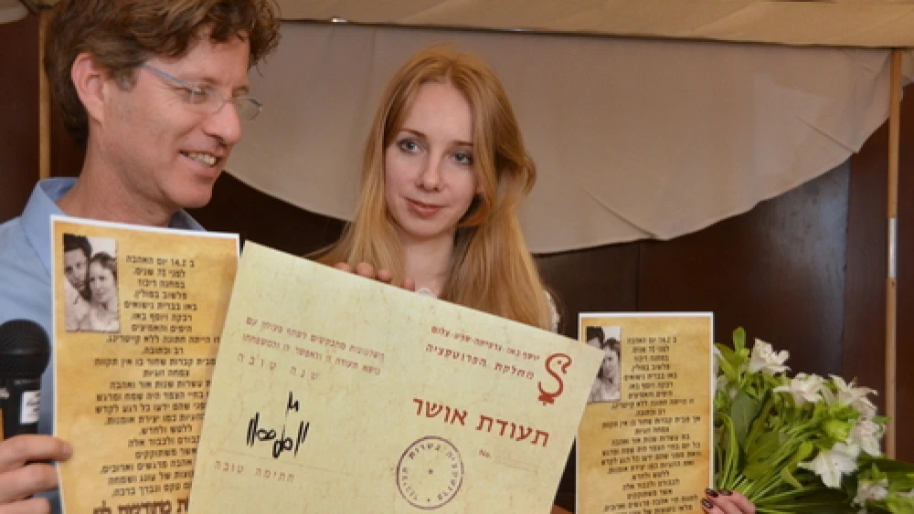 Boaz Bau-Simon, the grandson of Joseph and Rebecca Bau, with his fiancé Or (Irena) Gatina in February 2014. The couple announced its engagement at the ceremony commemorating the 70th wedding anniversary of Bau-Simon's grandparents. Bau-Simon and Gatina are pictured holding a "teudat osher" ("certificate of happiness") originally created by Joseph Bau as well as a letter relating the story of the lifelong romance of Joseph and Rebecca Bau. Credit: Maxine Dovere.