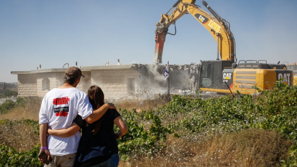 A couple views a tractor demolishing a home in the illegal Jewish neighborhood of Netiv Ha’avot in Gush Etzion, two days after residents were evicted, June 14, 2018. Photo by Gershon Elinson/Flash90.