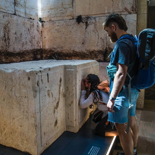 Shelly Sarah, a 22 year old Israeli from Hadera, stops at the Western Wall stone on display at Israel's Ben-Gurion International airport before a trip to Thailand as her boyfriend looks on, March 25, 2025. Credit: Rina Castelnuovo.