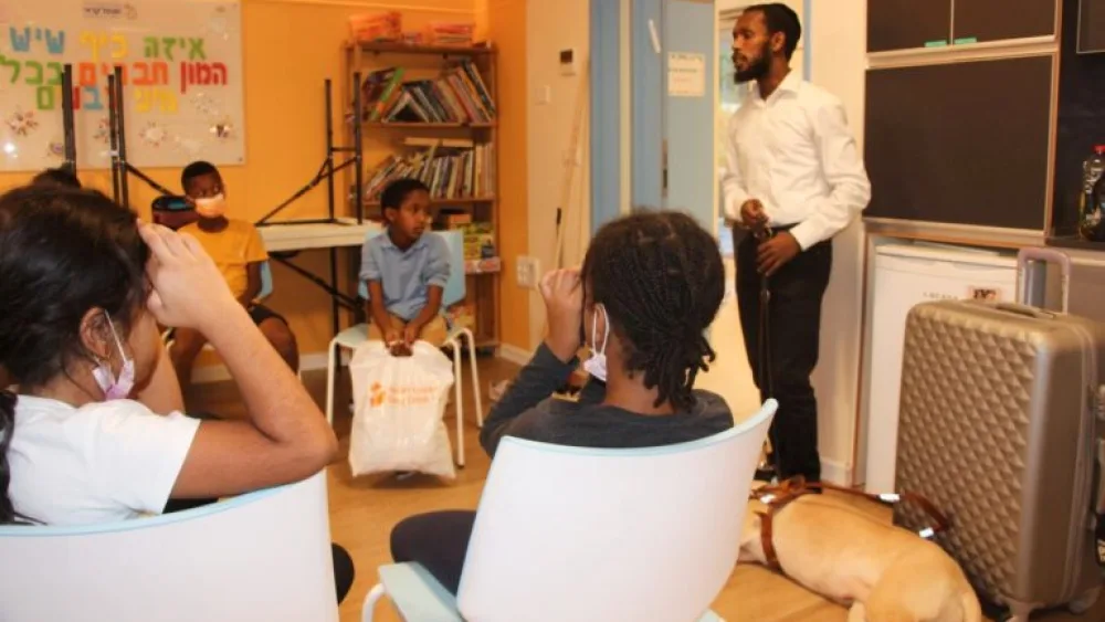 Avi Solomon speaking with children at Afikim, accompanied by his guide dog and a suitcase full of sports equipment for the blind. Photo by Judith Sudilovsky.