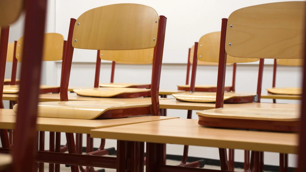 Chairs propped up on desks in an empty classroom. Credit: Taken/Pixabay.