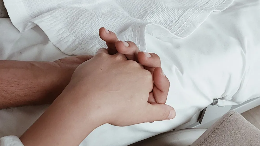 Close-up of two people holding hands on a hospital bed. Credit: Dilan Aktay/Pexels.