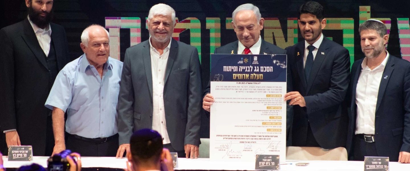 Israeli Prime Minister Benjamin Netanyahu holds up the umbrella agreement at a signing ceremony at the Maale Adumim Cultural Center. Also on stage (from left) are Ministry of Construction and Housing Director-General Yehuda Morgenstern, Housing Minister Haim Katz, former Maale Adumim Mayor Benny Kashriel, current Maale Adumim Mayor Guy Yifrach, and Finance Minister Bezalel Smotrich, Sept. 11, 2025. Photo by David Isaac.