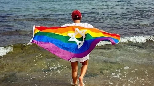 A Birthright Israel trip participant with a Jewish gay-pride flag parade on the Hilton Beach in Tel Aviv. Credit: Birthright Israel Facebook page.