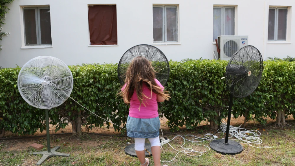 A young girl cools herself on a hot summer day by standing next to fans at the Zitan yishuv, on Aug. 15, 2012. Photo by Nati Shohat/Flash90.