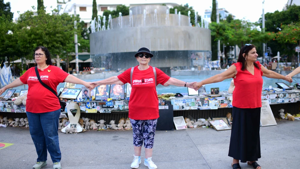 Israelis hold hands at Dizengoff Square in Tel Aviv, next to photographs of Israelis killed in the Oct. 7 massacre, on the one-year anniversary of the Hamas attack. Oct/ 7, 2024. Photo by Tomer Neubergi/Flash90.