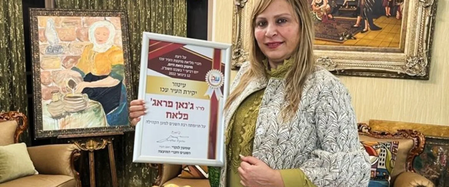 Dr. Janan Faraj Falah with her award from Akko City Hall. Her painting of a Druze woman is in the background. Photo courtesy of Janan Faraj Falah